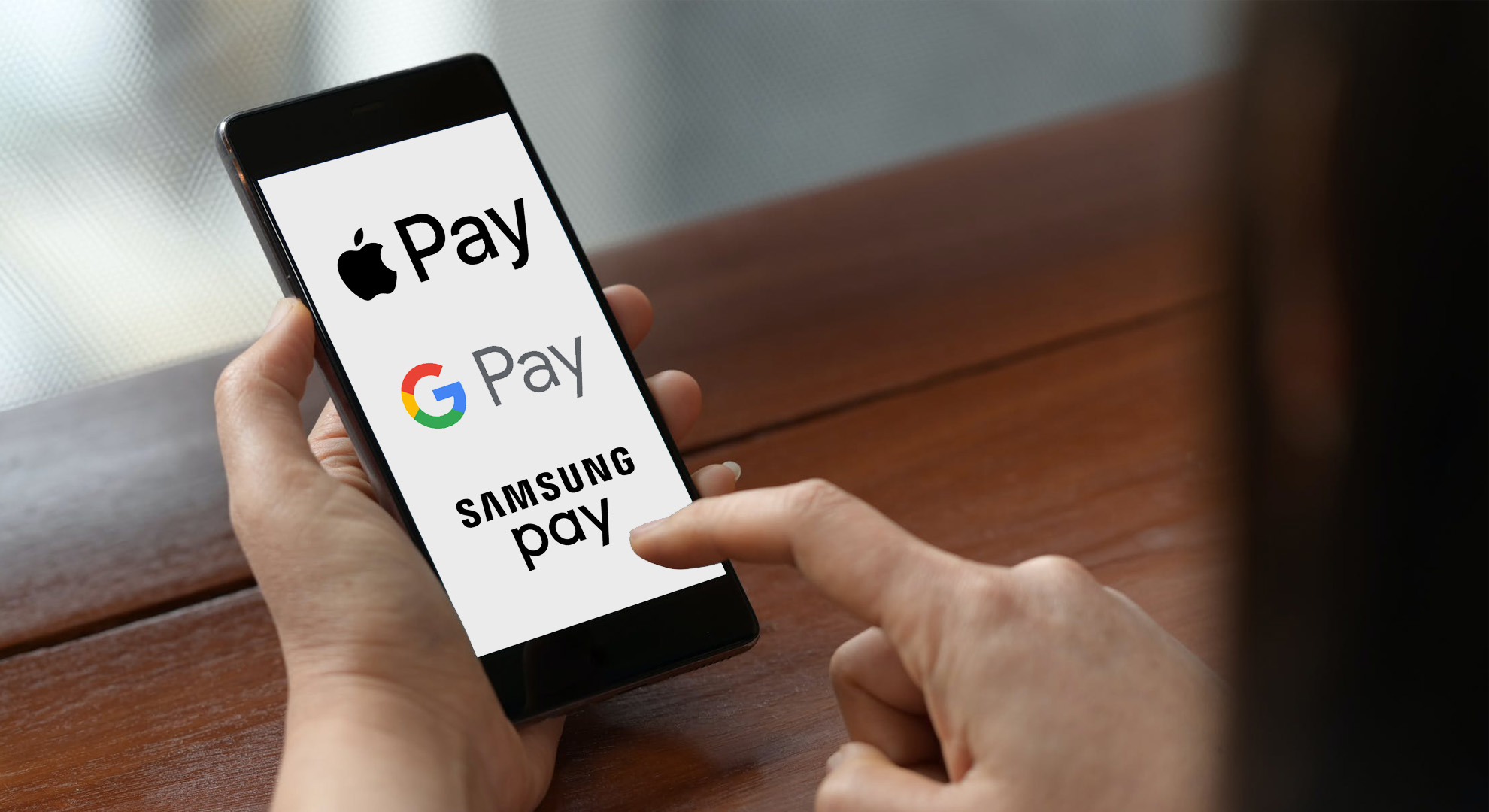 Person holding mobile phone in hand with the logos for Apple Pay, Samsung Pay, and Google Pay displayed